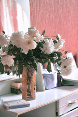 Large beautiful bouquet of peonies in a vase on a white dressing table in a woman's bedroom