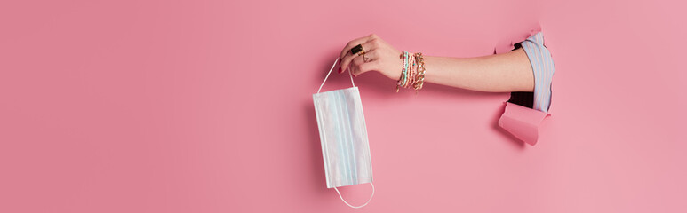 Partial view of woman holding protective mask near pink background with hole, banner