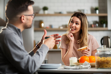 Happy girl enjoying in breakfast with her boyfriend. Loving young couple drinking coffee and eating sandwich at home.