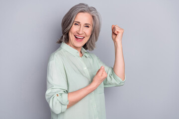 Photo of mature smiling good mood excited woman raise fists in victory success triumph isolated on grey color background