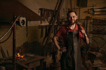Blacksmith with hammer in workshop confident portrait