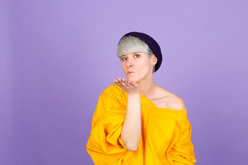 Stylish european woman on purple background smiling looking at the camera blowing a kiss with hand on air being lovely