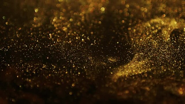 Golden Glitter Background In Slow Motion. Gold Particles On Black Background