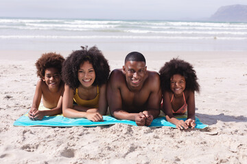 Portrait of african american parents and two children lying on a towel at the beach smiling
