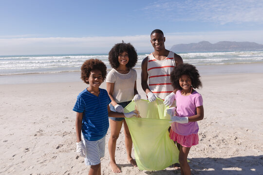 African american parents with two children collecting rubbish from the beach smiling