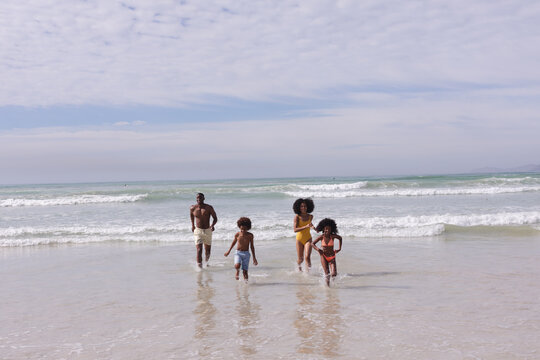 African american parents and two children running at the beach smiling