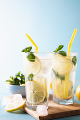 Two glass with lemonade or mojito cocktail with lemon and mint, cold refreshing drink or beverage with ice on blue background. Copy space