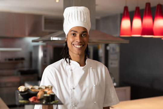 Portrait of mixed race professional chef wearing chefs hat serving sushi