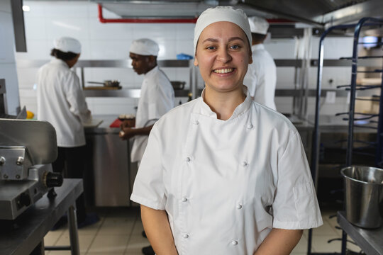 Portrait of caucasian female professional chef with diverse colleagues in background