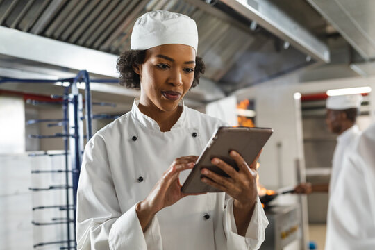 Portrait of mixed race female professional chef using tablet with colleague in background