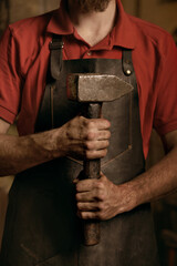 Blacksmith with hammer in hands in workshop