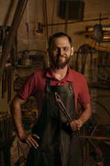 Blacksmith with metal tongs in smithy portrait