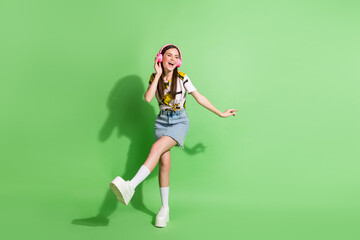Fototapeta na wymiar Full length photo of attractive cheerful young woman look empty space dance wear headphones isolated on green color background