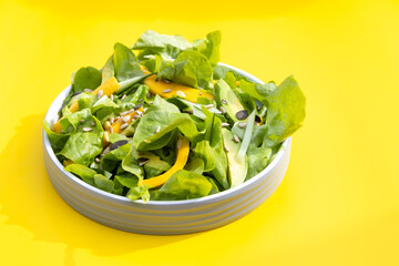 Salad with mango, avocado,cucumber, lettuce and seeds on yellow background .Home made, tasty food. Concept for a tasty and healthy meal. Copy space
