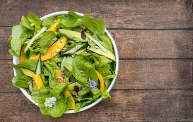 Salad with mango, avocado, cucumber, seeds and flowers on wood backround ,copy space