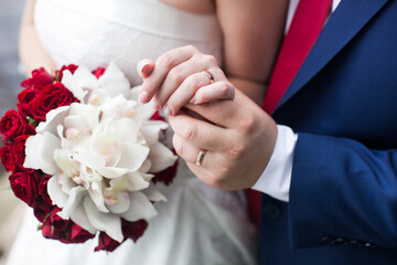 Obraz na płótnie Canvas Newlywed couple showing wedding rings on their fingers. Groom holding palm of his bride, wedding bouquet of flowers on the background