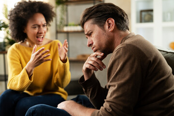 Frustrated young couple arguing at home. Stressed unhappy wife and husband sitting on cauch at home..