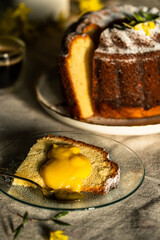 Homemade traditional lemon and pear bundt cake, piece of cake with lemon curd, coffee and forsythia flowers on linen tablecloth .