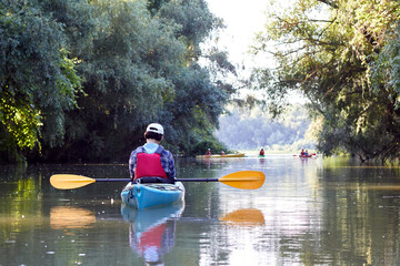 Girl with paddle and blue kayak on a small river in rural landscape at summer