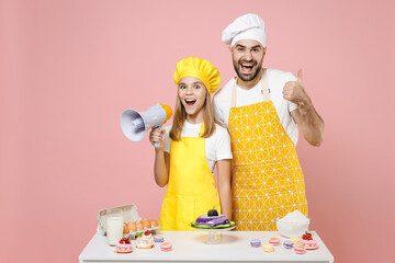 Teen fun girl dad father chef cook confectioner baker in yellow apron cap at table scream in megaphone show thumb up gesture isolated on pink background Mousse cake food workshop master class process.