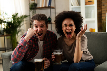 Boyfriend and girlfriend drinking beer at home. Happy couple watching sports game on tv.
