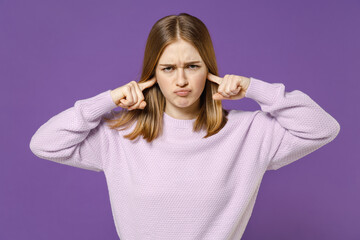 Young igrnoring strict irritated sad stressed student woman 20s wearing purple knitted sweater covering ears with fingers hands isolated on violet color background studio People lifestyle concept.