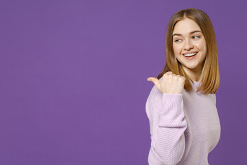 Young smiling happy cheerful friendly student caucasian woman 20s wearing purple knitted sweater point thumb finger back aside on workspace area mock up isolated on violet background studio portrait