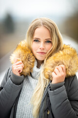 Portraits of a young blonde woman who hugs her fur collar gently..