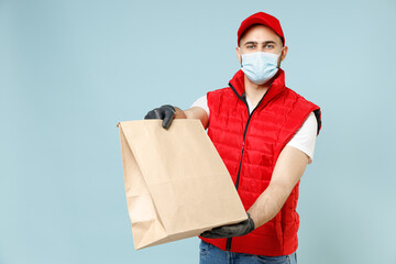 Fototapeta na wymiar Delivery guy employee man in red cap white tshirt vest uniform sterile face mask gloves work courier service on lockdown covid hold blank craft paper takeaway bag isolated on pastel blue background