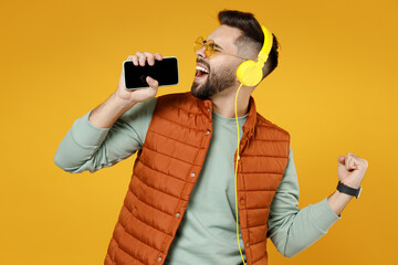 Young fun man 20s years old wear orange vest mint sweatshirt glasses headphones singing song in...