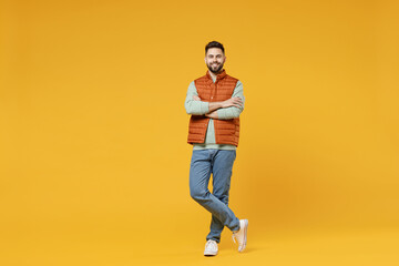 Full length young smiling happy confident smiling cheerful fun caucasian man 20s years old wearing orange vest mint sweatshirt hold hands crossed folded isolated on yellow background studio portrait