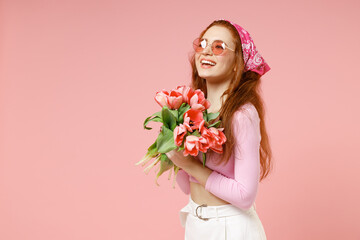 Side view of young smiling fun happy romantic woman 20s wearing rose clothes bandana glasses hold tulips flowers bouquet isolated on pastel pink color background studio portrait Spring season concept