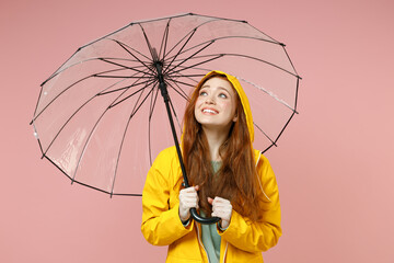 Redhead young pensive woman 20s in yellow waterproof raincoat hood outerwear hold transparent...