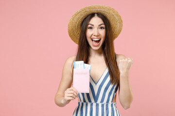 Traveler tourist woman in summer clothes hat hold passport tickets do winner gesture clench fist isolated on pastel pink background Passenger travel abroad weekends getaway Air flight journey concept.