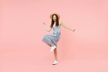 Full length young happy woman in summer clothes striped dress straw hat do winner gesture clench fist with raised up leg isolated on pastel pink background studio portrait. People lifestyle concept.