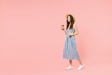 Full length side view young smiling happy woman in summer clothes striped dress straw hat holding paper plastic cup of coffee or hot tea walk isolated on pastel pink color background studio postrait.