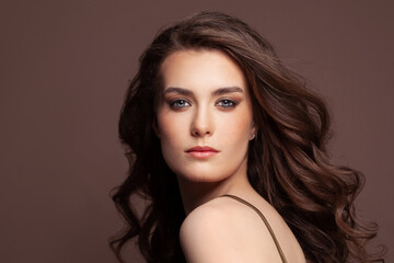 Fototapeta premium Portrait of attractive fashion model woman brunette with clear skin and healthy curly hair. Pretty woman with natural makeup on brown