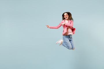 Fototapeta na wymiar Full length young smiling happy trendy woman in pastel pink clothes glasses jump high point index finger aside on workspace area mock up isolated on blue background studio People lifestyle concept