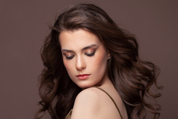 Fototapeta premium Portrait of lovely woman brunette with clear skin and healthy wavy hairstyle on brown background. Beautiful woman with closed eyes and natural makeup