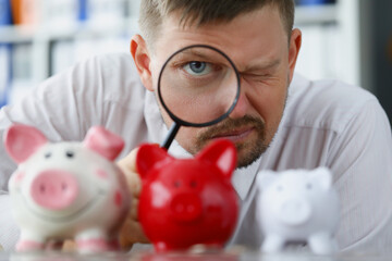 Man looks through magnifying glass at piggy bank