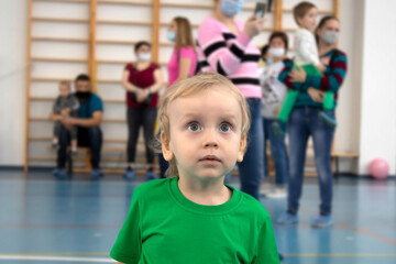 A child stands in the gym next to masked people.