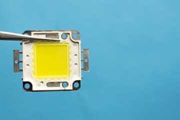 Led chip isolated on blue background. Hand holding diode. Save energy concept.