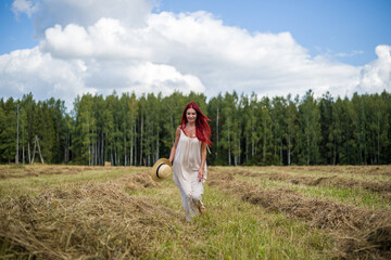 young woman with long red flowing hair in a white dress runs across the field