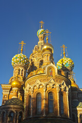 Fototapeta na wymiar St. Petersburg. Beautiful domes of Cathedral of Savior on Spilled Blood (Spas na Krovi) against the background of a blue sky and ornate exterior with masaic icons on walls of church in sunset light