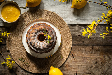 Homemade traditional lemon and pear bundt cake with lemons and forsythia on rustic table.