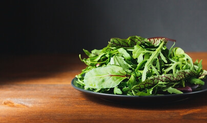 Mix of fresh green salad leaves with arugula, lettuce, spinach and beets on wooden rustic background