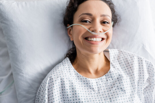top view of smiling african american woman with nasal cannula lying in hospital bed