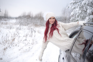 Fototapeta na wymiar Young beautiful girl looks out sits from the window of the car in winter. Winter travel car girl with red hair road