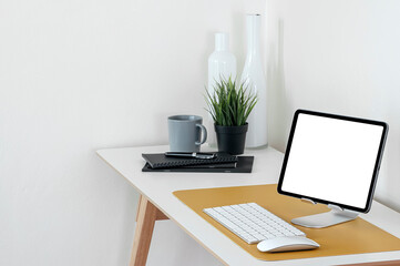 Mockup blank screen tablet with supplies on wooden table in white room.
