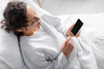 overhead view of diseased african american woman holding smartphone with blank screen in clinic